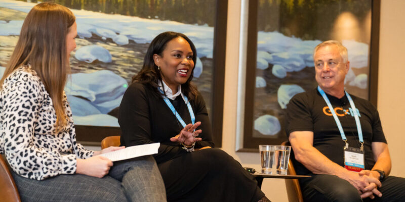 Three people sit in chairs talking in front of an audience