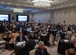 Hundreds of people sit at small tables in one-on-one meetings in a large ballroom.