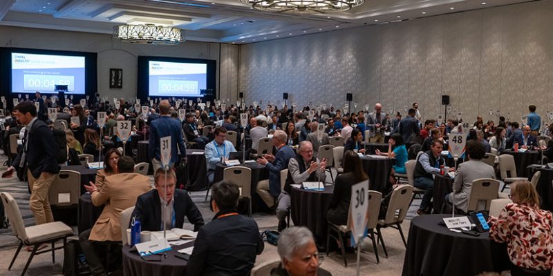 Hundreds of people sit at small tables in one-on-one meetings in a large ballroom.