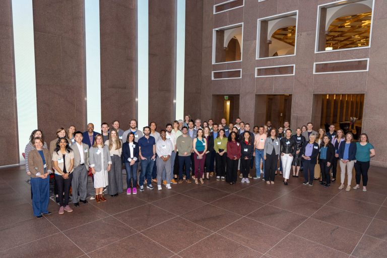 IN2 Channel Partner Meeting A group of 60 people in business dress pose in a large indoor lobby.