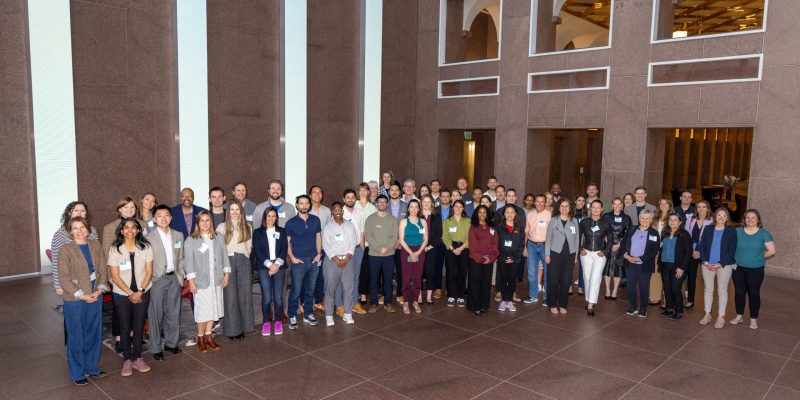 A group of 60 people in business dress pose in a large indoor lobby.