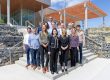 Fifteen people stand on steps outside a building and smile for the camera.